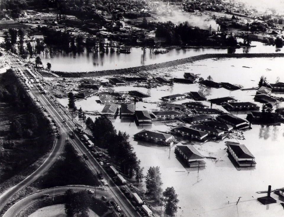 Photo of apartment buildings from Vanport wallow in floodwaters near North Denver Avenue. Buses can be seen on the road, lining up to pick up people fleeing the doomed city.