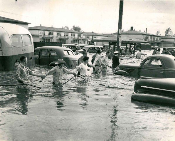 Photo of people holding on to a rope to navigate through floodwaters during 1948 Vanport flood, surrounded by abandoned and floating cars